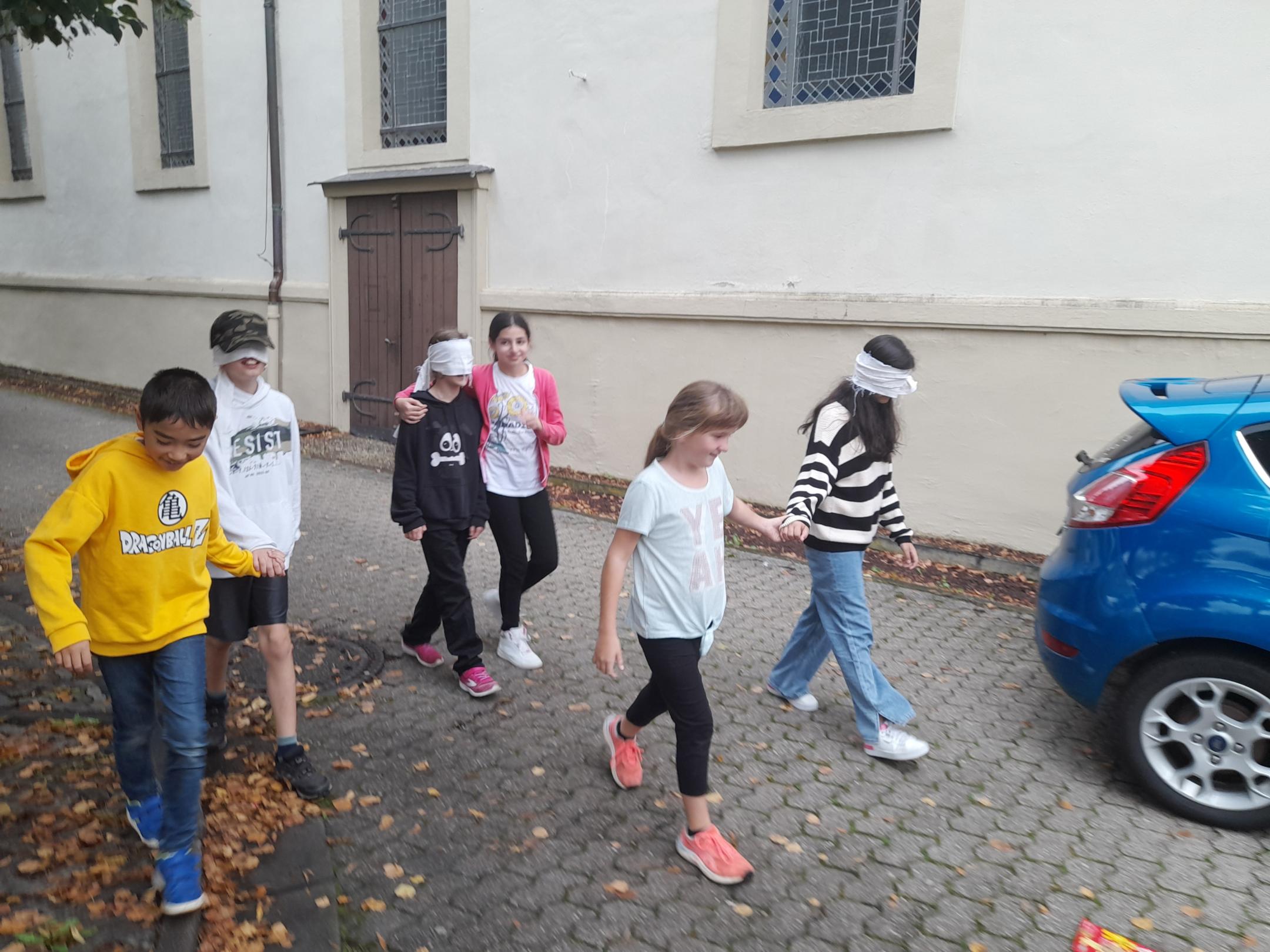 Jugendliche gehen zu zweit. Ein der der Paar hat die Augen verbunden. Der andere führt.