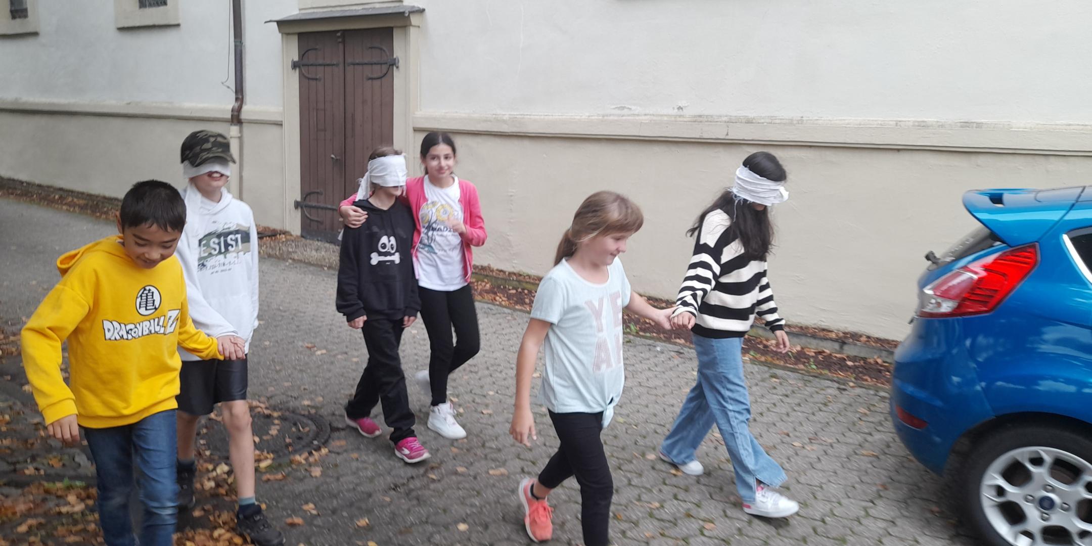 Jugendliche gehen zu zweit. Ein der der Paar hat die Augen verbunden. Der andere führt.