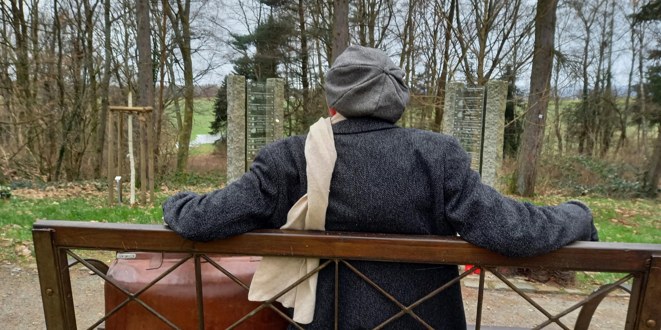 Ein Mann sitzt auf der Bank in einem Friedhof.