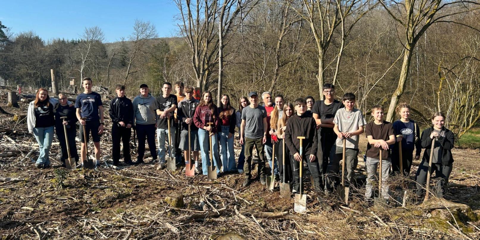 Jugendliche stehen im Wald für eine Baumpflanzaktion