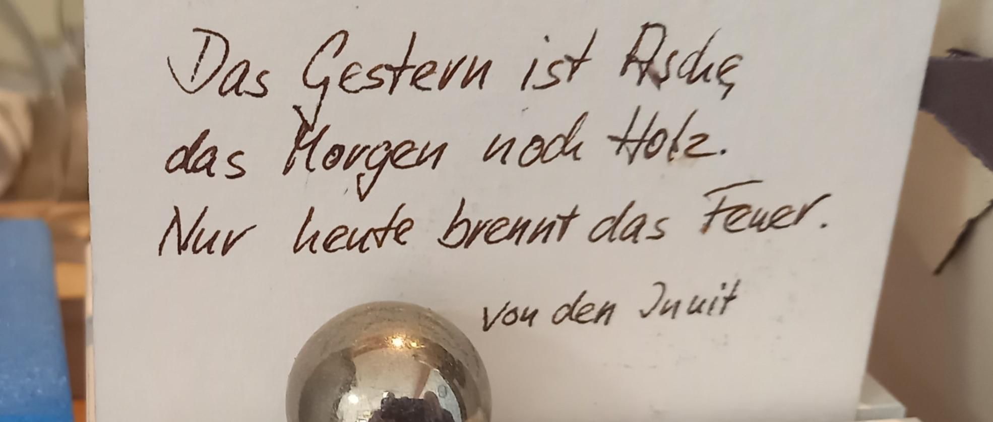 Auf einem Zettel steht ' Das Gestern ist Asche, das Morgen noch Holz. Nur heute brennt das Feuer'