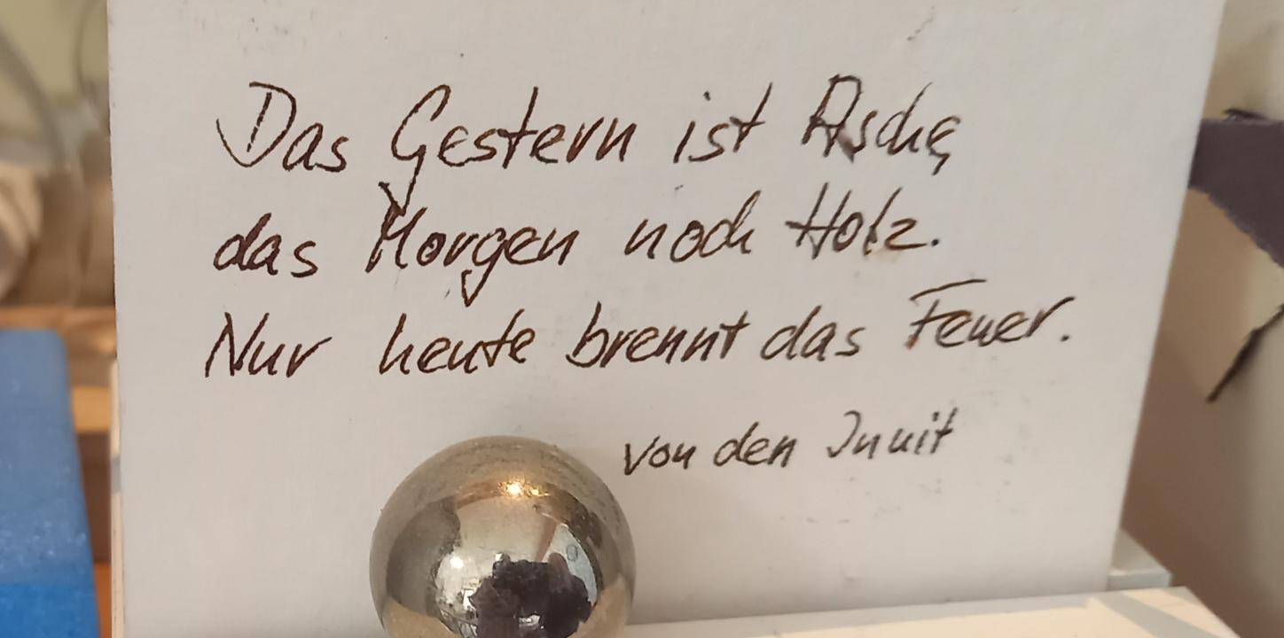 Auf einem Zettel steht ' Das Gestern ist Asche, das Morgen noch Holz. Nur heute brennt das Feuer'