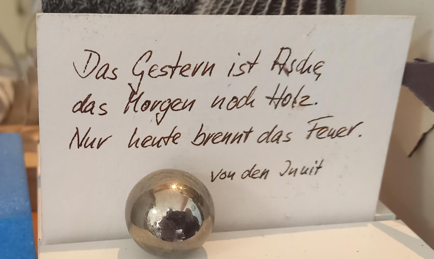 Auf einem Zettel steht ' Das Gestern ist Asche, das Morgen noch Holz. Nur heute brennt das Feuer'