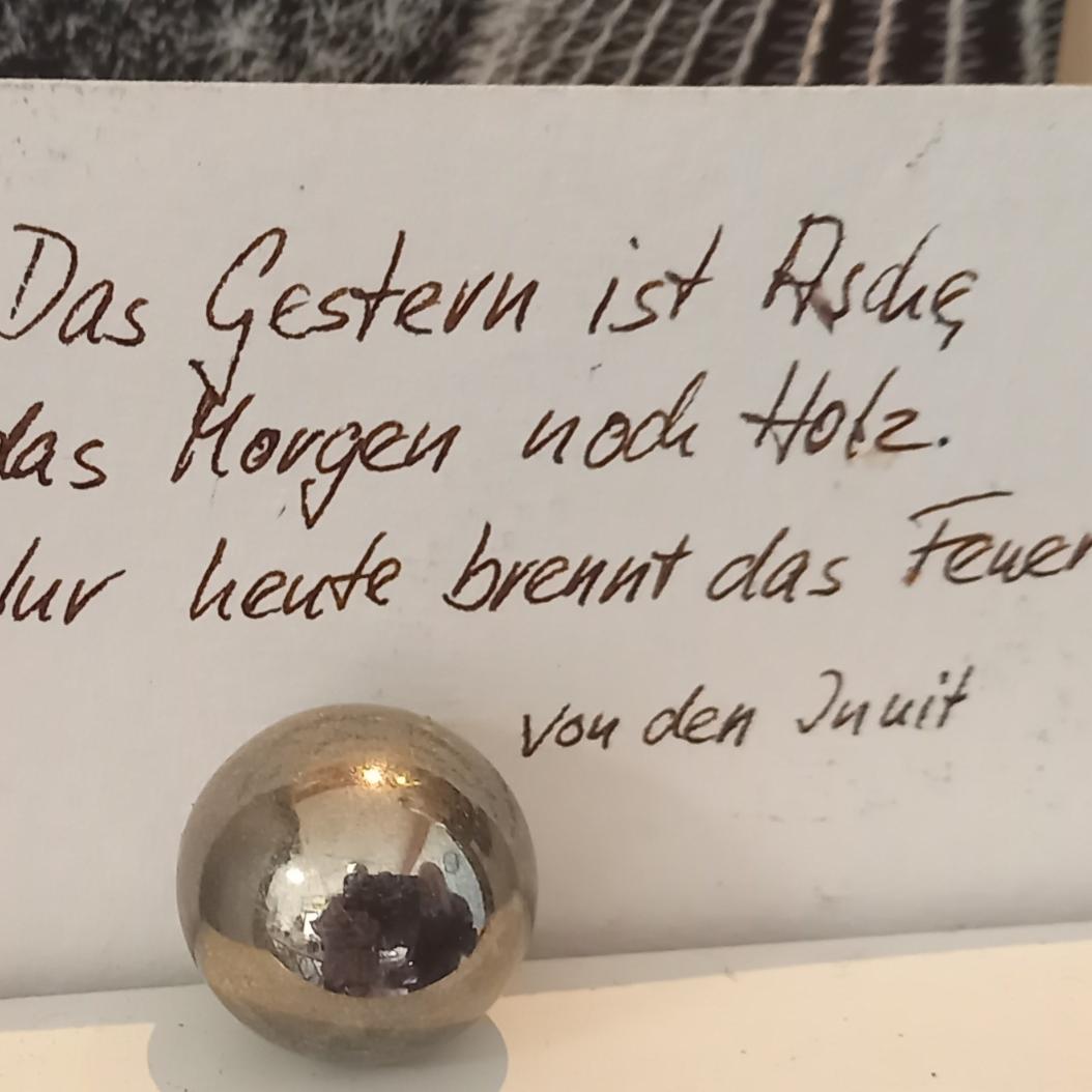 Auf einem Zettel steht ' Das Gestern ist Asche, das Morgen noch Holz. Nur heute brennt das Feuer'