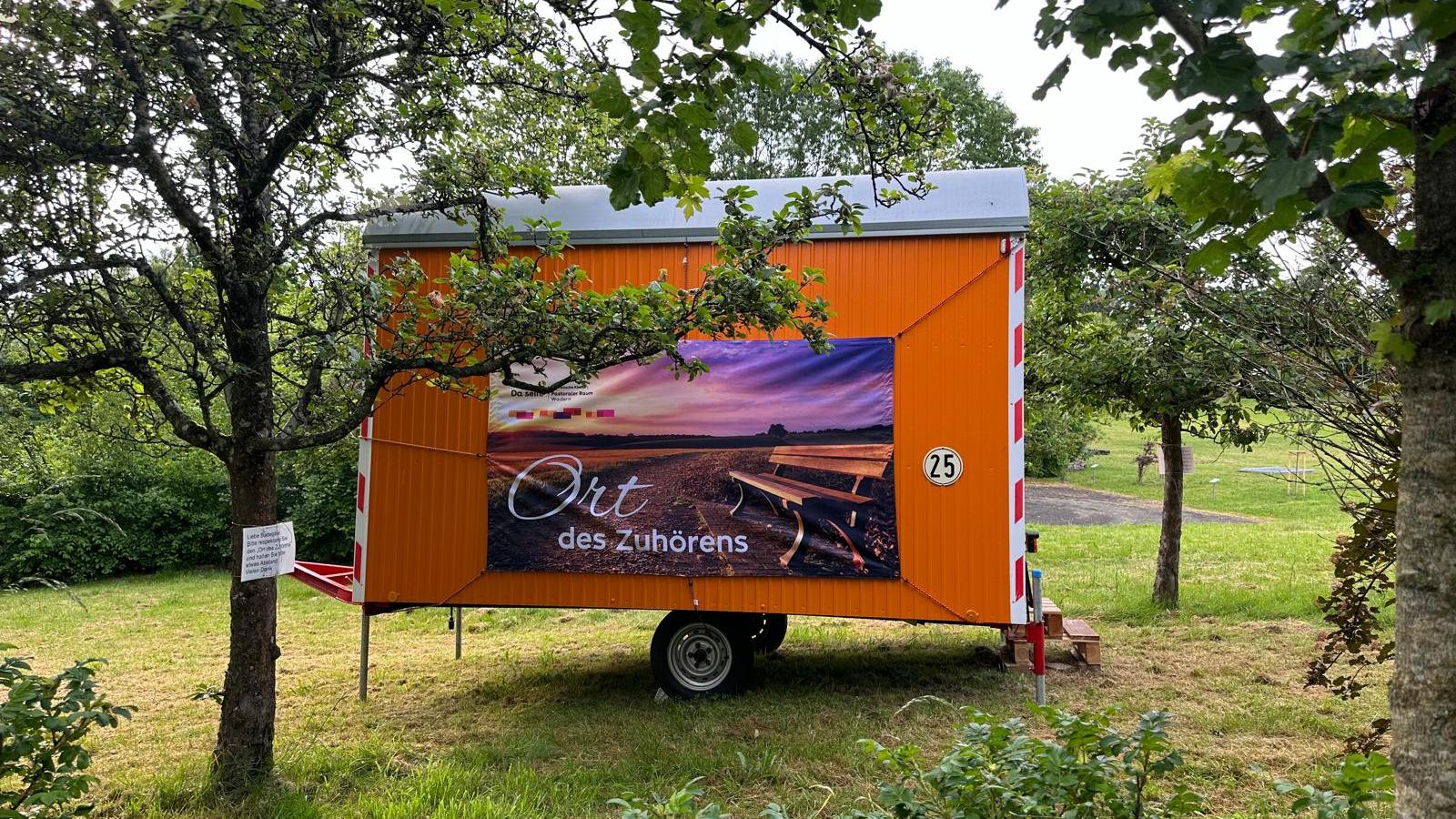 Bauwagen vor dem Losheimer Stausse mit dem Plakat 'Ort des Zuhörens'