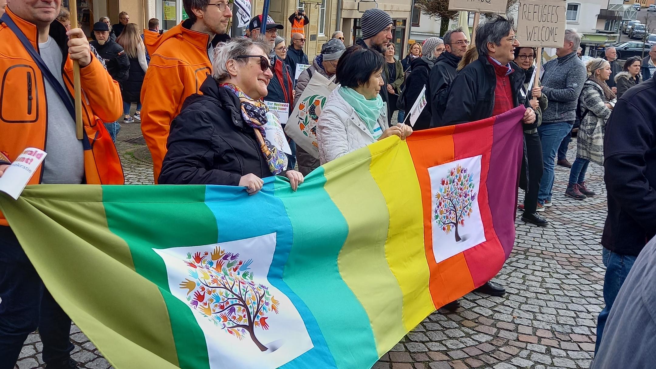 Menschen tragen ein Banner mit dem Zeichen von Hochwald soll bunt bleiben bei der Demo in Wadern