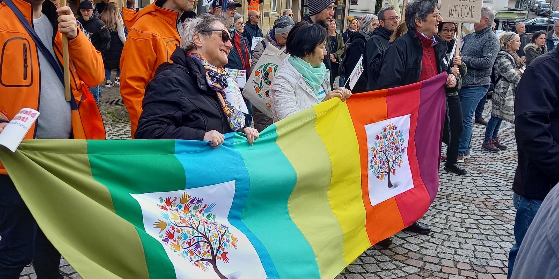 Menschen tragen ein Banner mit dem Zeichen von Hochwald soll bunt bleiben bei der Demo in Wadern