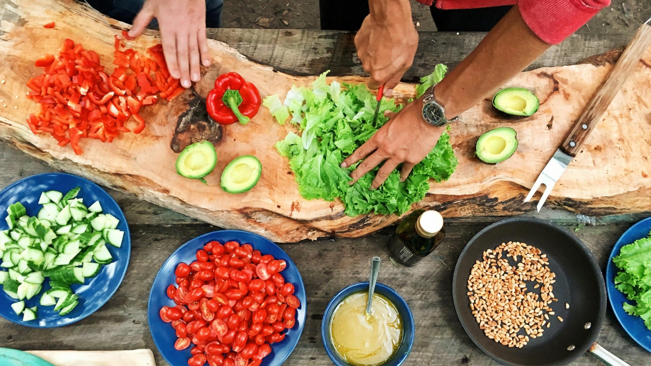 auf einem Tisch sieht man Teller und Schalen mit verschiedenen Essenzutaten, dazu drei verschiedene Hände