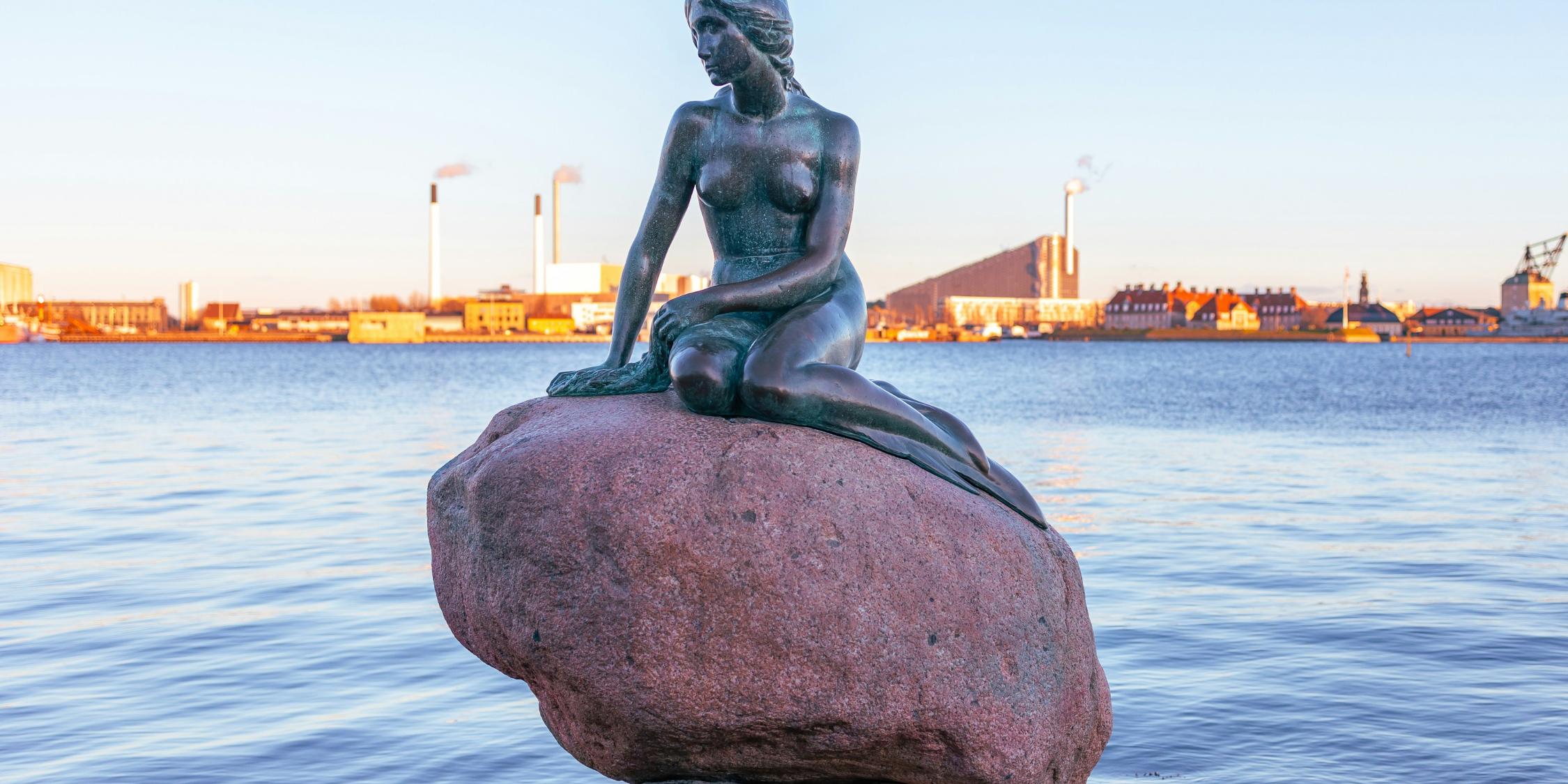 Auf einem Stein am Meer sitzt die Metallskulptur einer Meerjungfrau