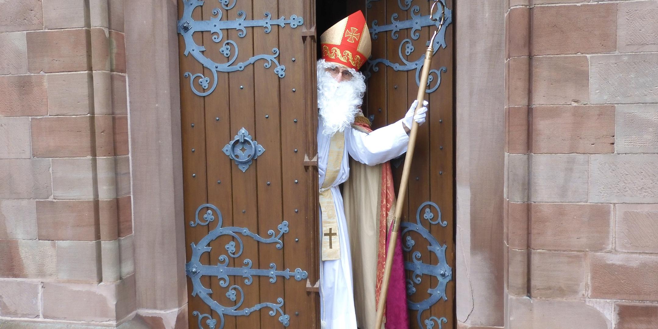 Ein verkleideter Nikolaus kommt aus einer Kirchentüre einem entgegen