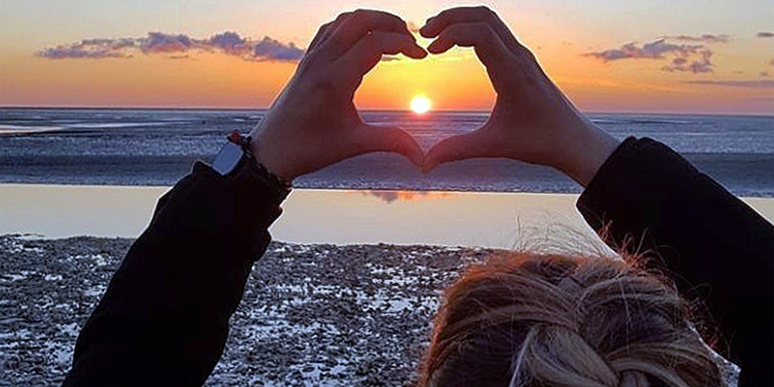 ein Herz, aus Händen geformt, umschließt einen Sonnenuntergang