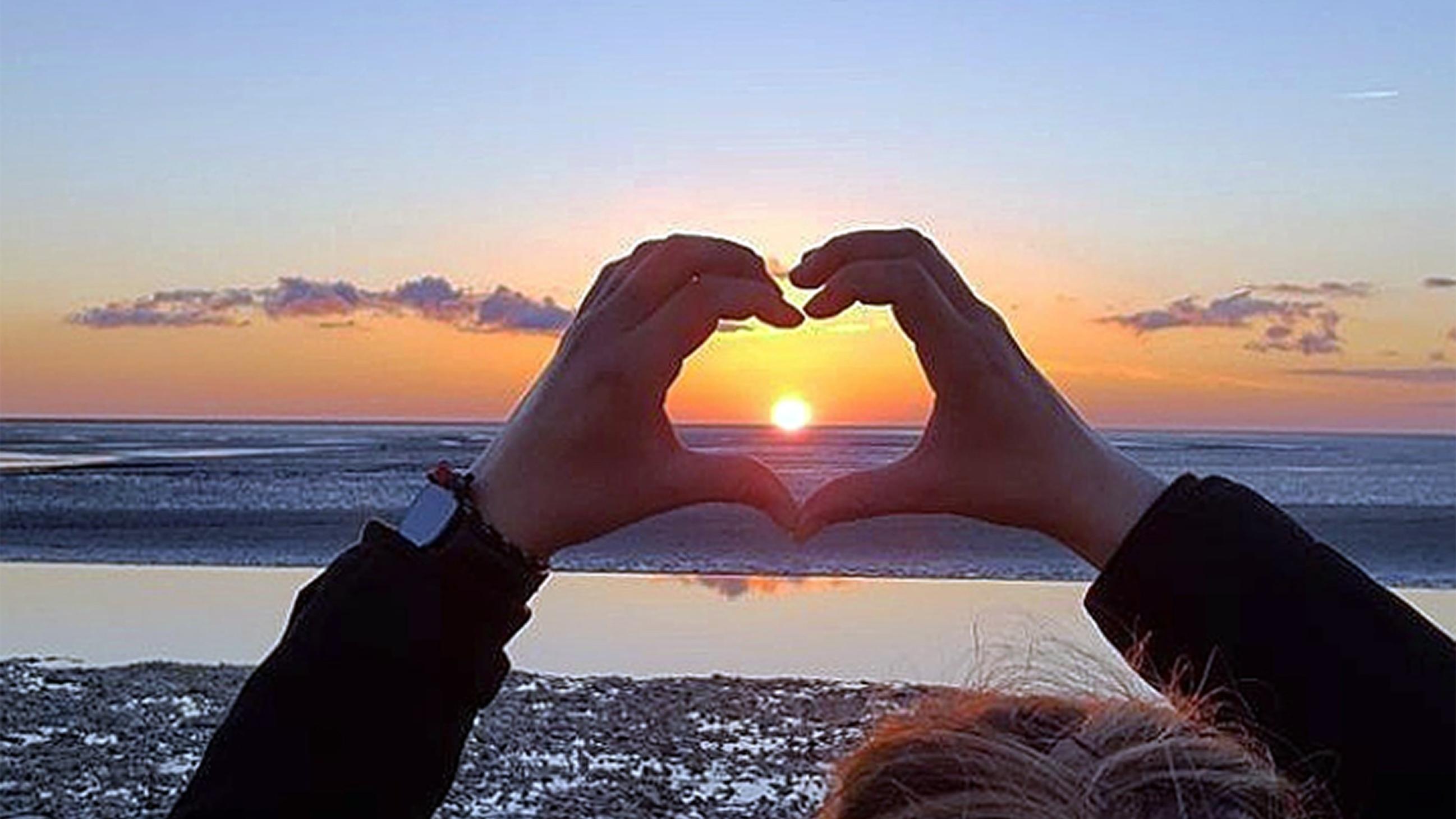 ein Herz, aus Händen geformt, umschließt einen Sonnenuntergang