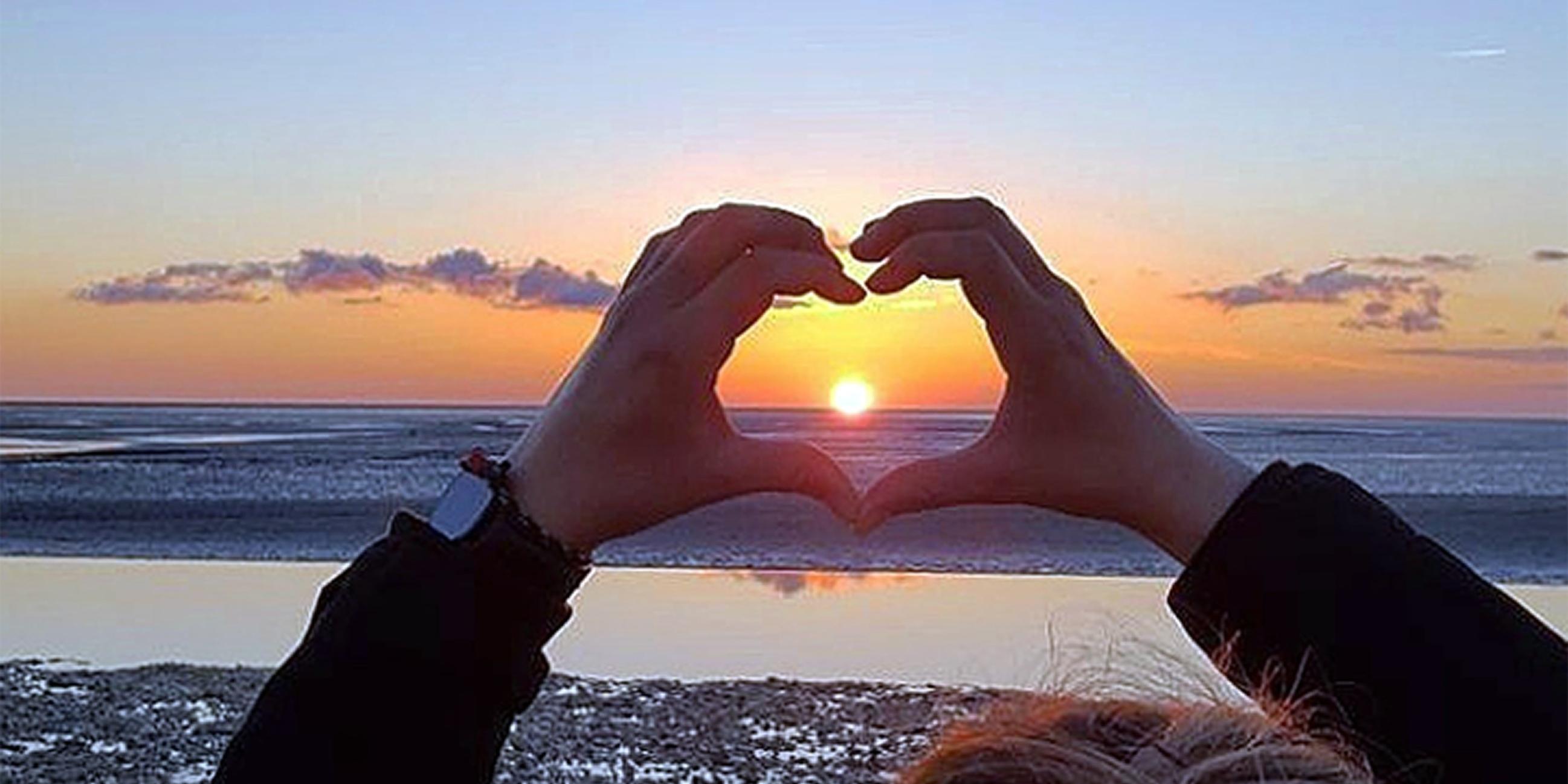 ein Herz, aus Händen geformt, umschließt einen Sonnenuntergang