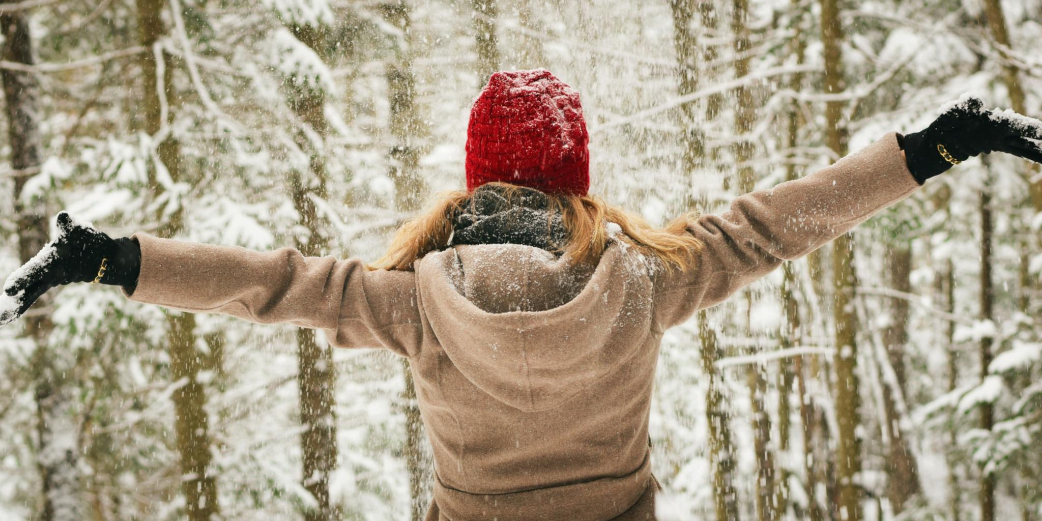 Eine junge Frau steht in Winterkleidern mit ausgebreiteten Armen vor der Winterlandschaft